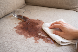  Large liquid spill on a fabric couch with a hand gently blotting the area using a cloth to prevent spreading.