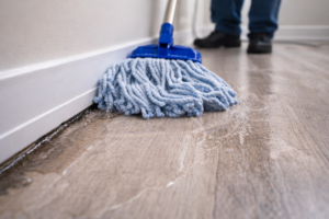 Wet mop pushing water toward baseboards, showing moisture spreading across a floor instead of being removed