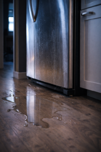Water pooling on the floor beneath a refrigerator, suggesting an internal leak rather than surface condensation